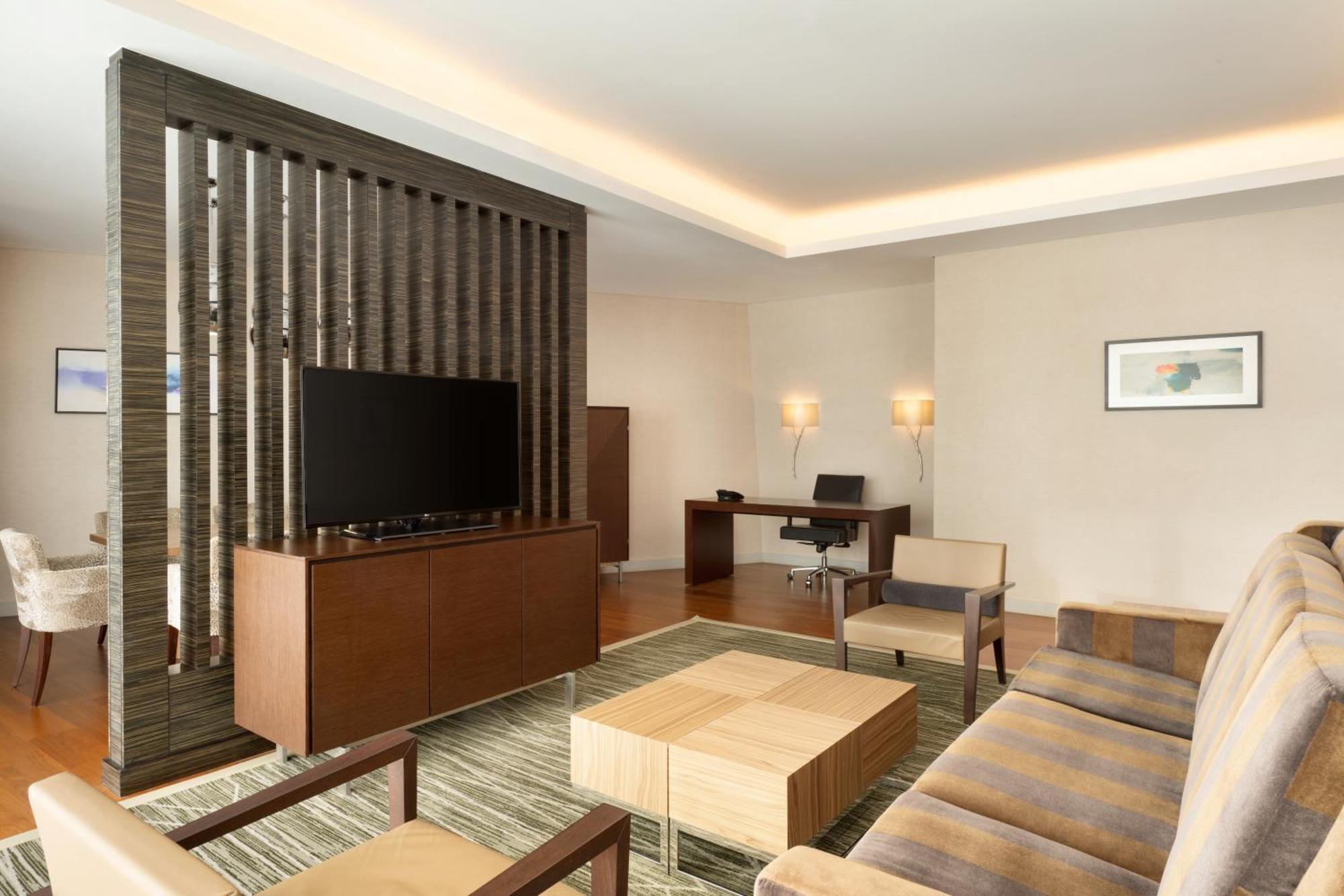 Hilton Riyadh Hotel & Residences Ngoại thất bức ảnh The photo shows a modern living space that features a contemporary design. It includes a seating area with a beige sofa and two armchairs arranged around a square wooden coffee table. A wall-mounted flat-screen TV is positioned on a decorative wooden